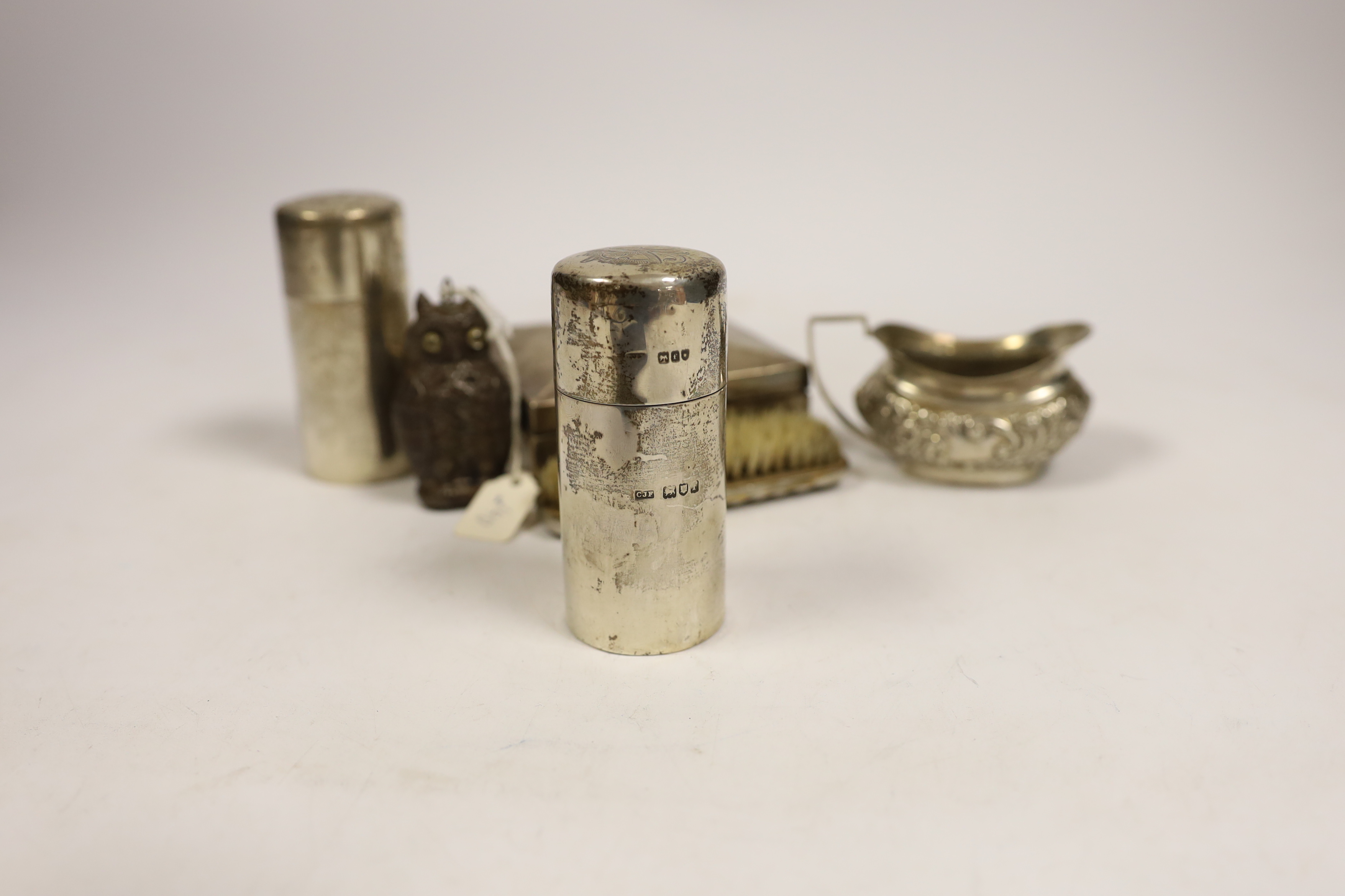 A late Victorian embossed silver cream jug, a pair of silver toilet bottles, a silver backed brush, a silver cigarette box and two other items.